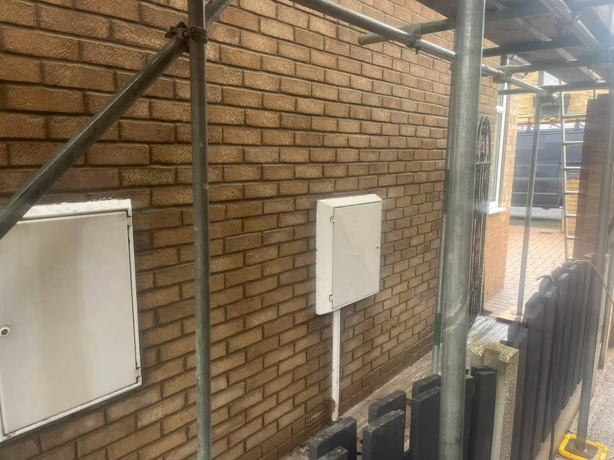 Buff brick wall with gas and electric meter boxes set into the brickwork, scaffolding in front