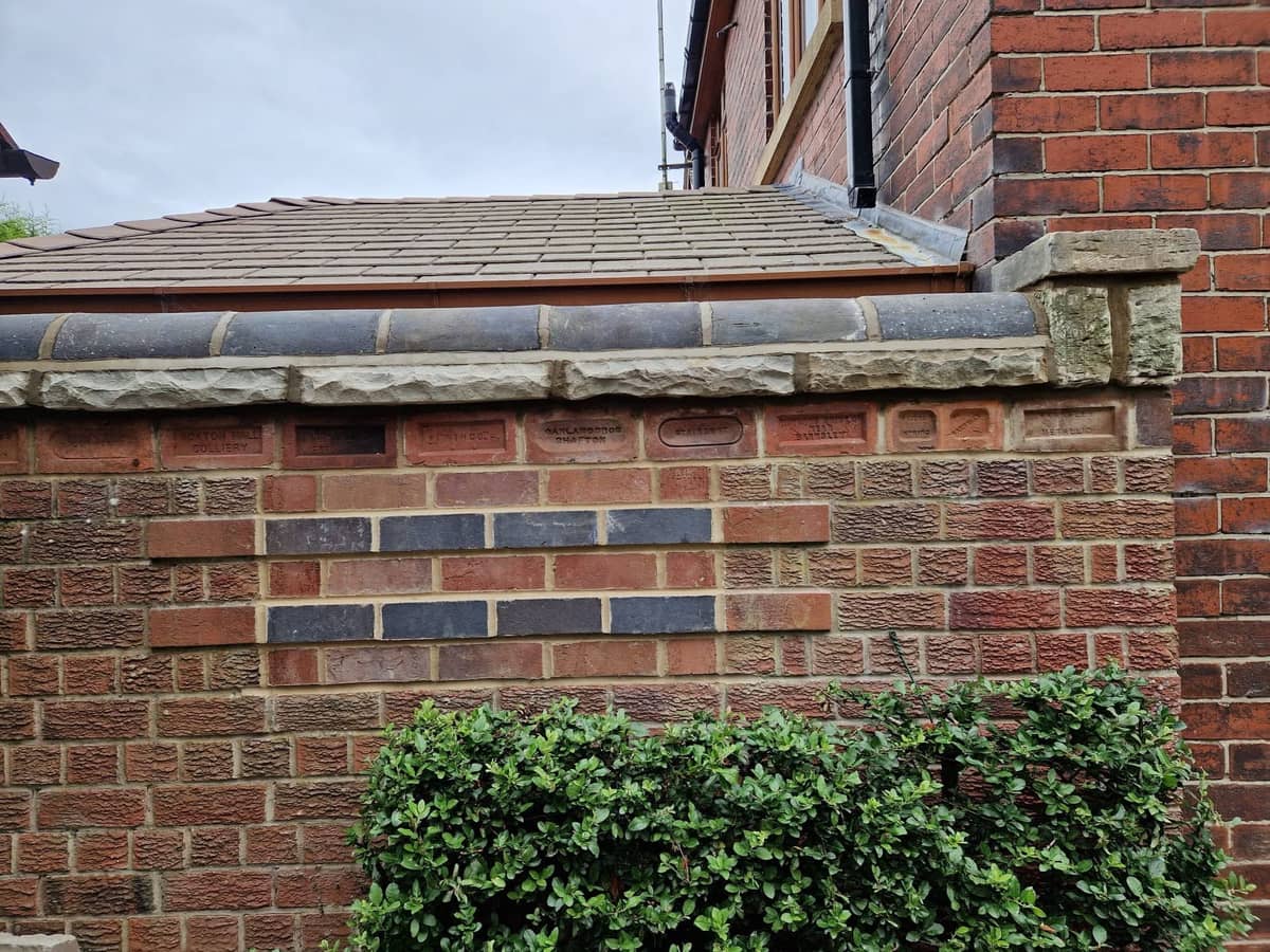 Red brick garden wall with a band of blue bricks and a stone coping