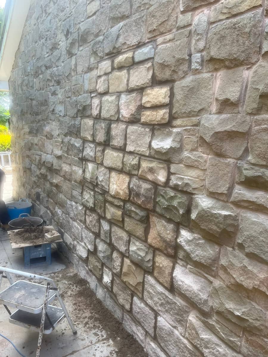 The full height of a coursed sandstone gable with fresh joints, a barrow and tubs below
